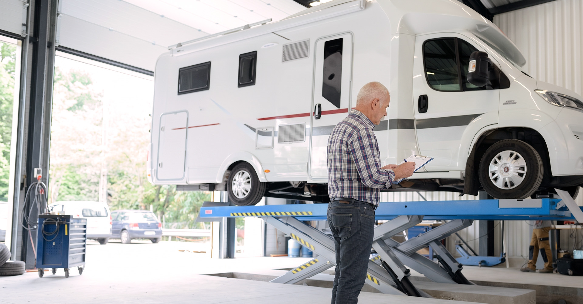 RV raised on a service lift while a technician reviews an inspection checklist